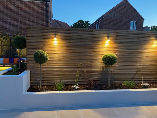 Symbol Gardens Services at night time with white stone walls and planted shrubs